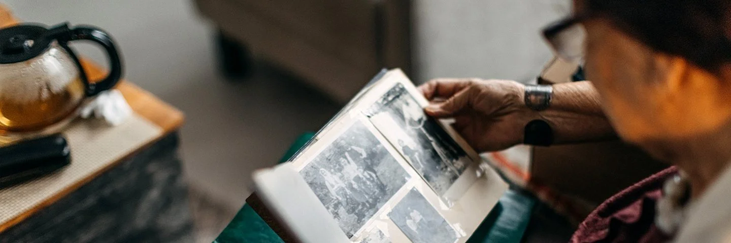 Eine ältere Frau schaut sich alte Schwarz-Weiß-Fotos in einem Fotoalbum an.