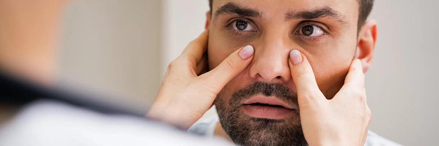 Eine Person tastet die Nasennebenhöhlen eines Mannes ab – es besteht der Verdacht auf eine Nasennebenhöhlenentzündung.
