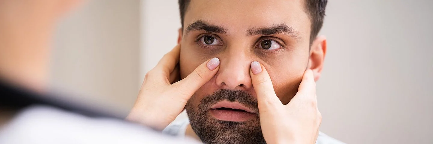 Eine Person tastet die Nasennebenhöhlen eines Mannes ab – es besteht der Verdacht auf eine Nasennebenhöhlenentzündung.