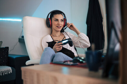 Frau sitzt mit Headset auf einem Sessel und spielt ein Videospiel.