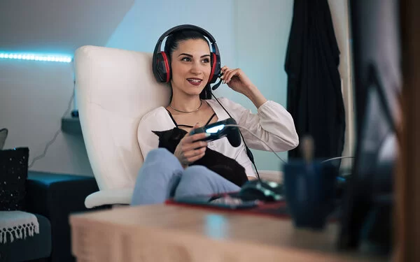 Frau sitzt mit Headset auf einem Sessel und spielt ein Videospiel.