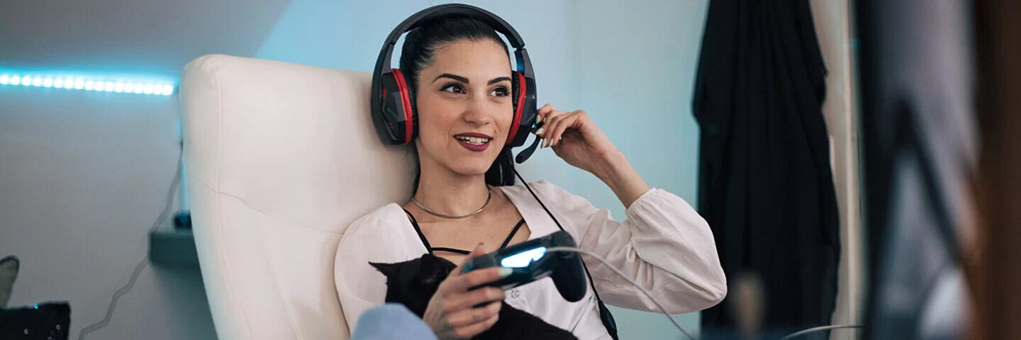 Frau sitzt mit Headset auf einem Sessel und spielt ein Videospiel.