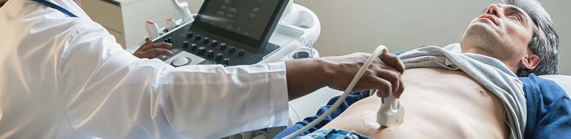 Ein Gastroenterologe untersucht den Bauchraum eines Mannes mit einem Ultraschallgerät.