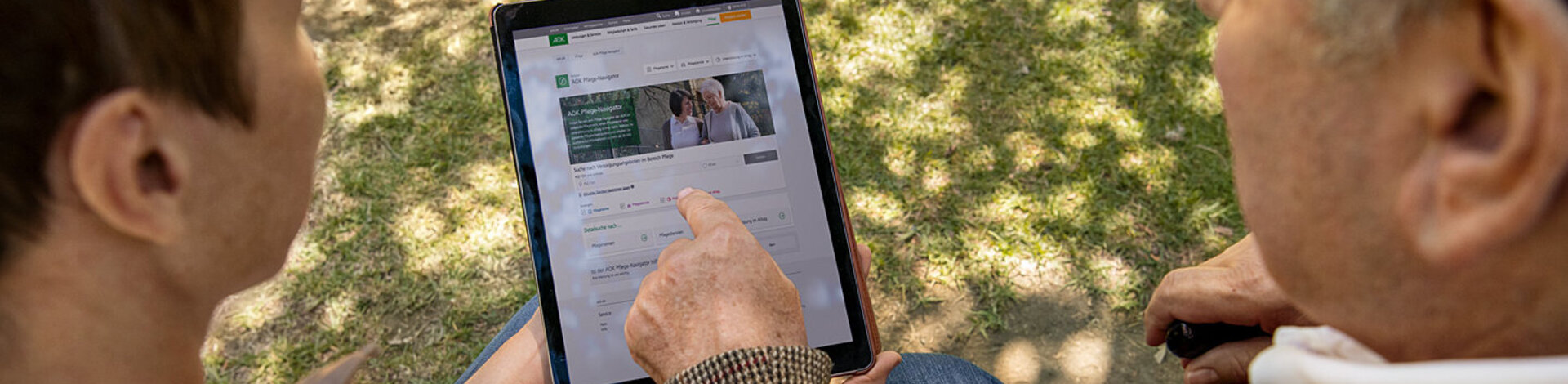 Ein älterer und ein jüngerer Mann lesen Texte auf einem Tablet-Computer. Die AOK informiert mit gedruckten Magazinen und auch digital.