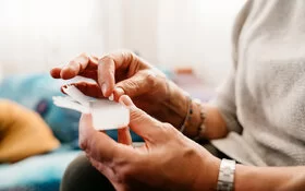 Eine ältere Person mit Schmerzen hat eine Tablettendose in der Hand.