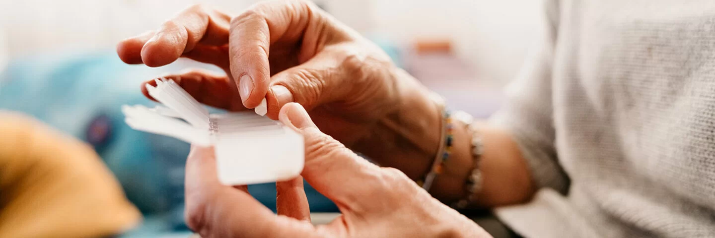 Eine ältere Person mit Schmerzen hat eine Tablettendose in der Hand.