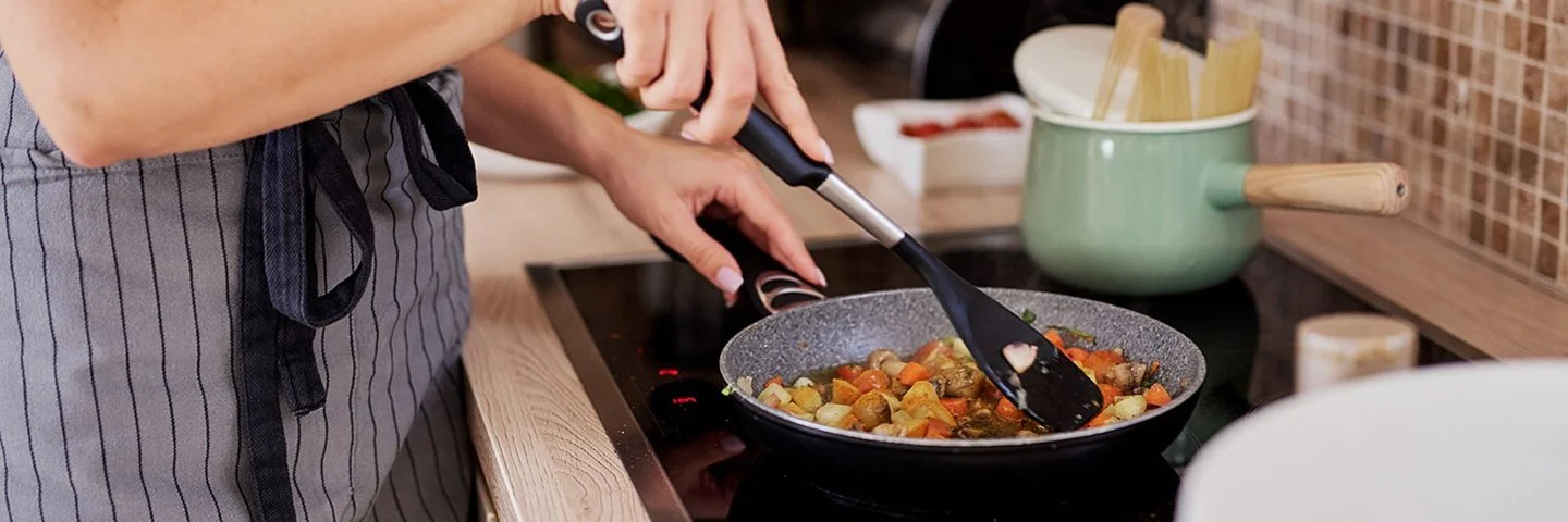 Eine Frau rührt mit einem schwarzen Plastiklöffel ein Pfannengericht um.