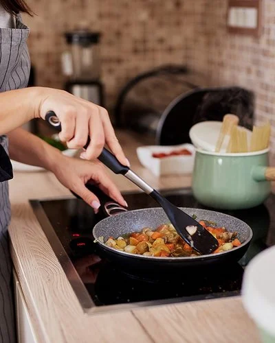 Eine Frau rührt mit einem schwarzen Plastiklöffel ein Pfannengericht um.