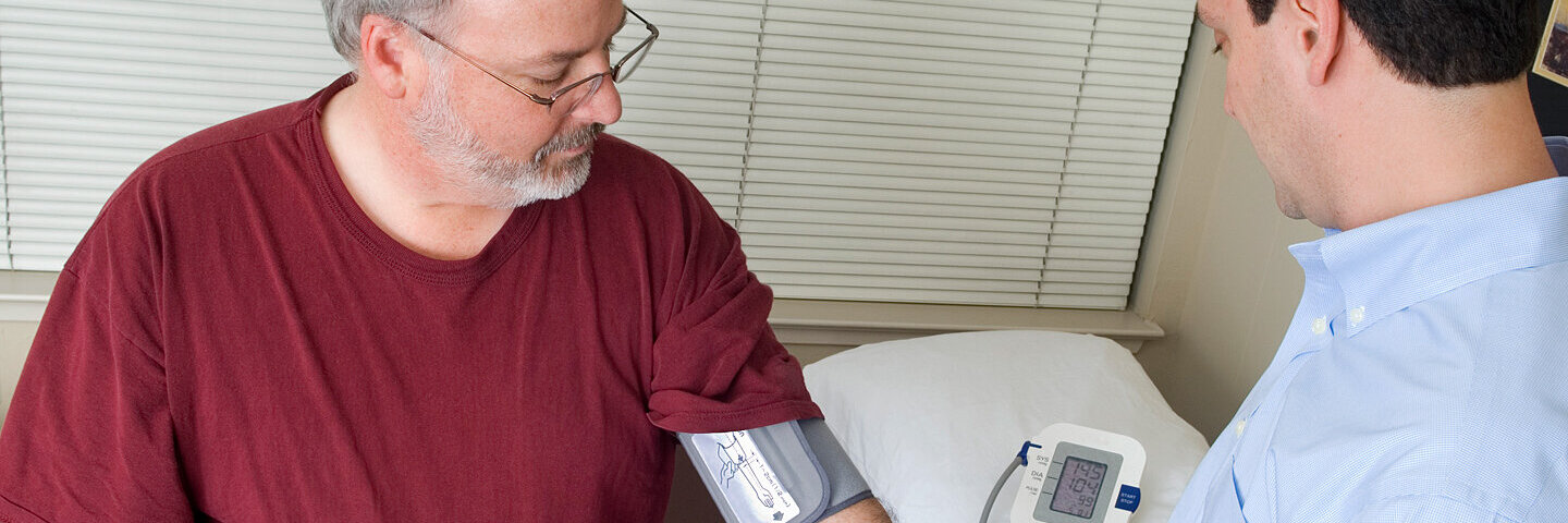 Ein Arzt misst den Blutdruck bei einem älteren Mann mit Übergewicht.