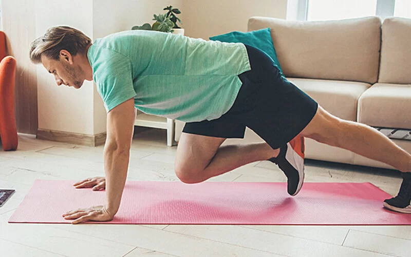 Ein Mann macht Sportübungen auf einer Matte in seinem Wohnzimmer. 