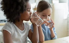 Zwei Kinder trinken Wasser aus Gläsern.