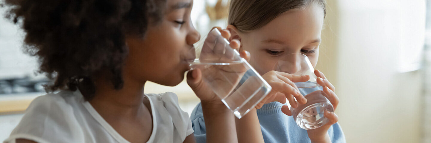 Zwei Kinder trinken Wasser aus Gläsern.