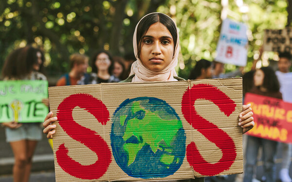 Eine junge Umweltaktivistin hält ein selbst gemaltes Schild mit “SOS” hoch – die Erde stellt das O dar.