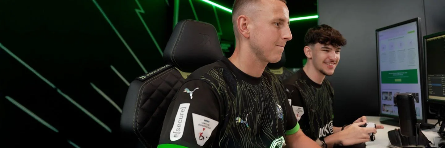 Zwei junge Männer sitzen vor mehreren Computermonitoren und spielen ein Computerspiel.