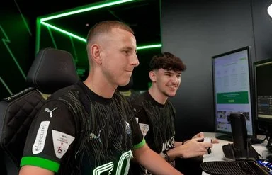 Zwei junge Männer sitzen vor mehreren Computermonitoren und spielen ein Computerspiel.