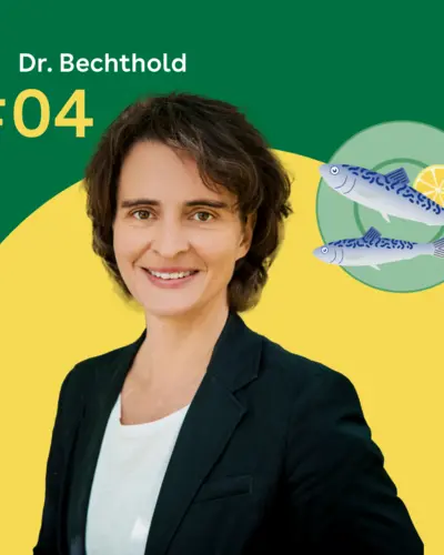 Dr. Angela Bechthold steht vor einem grünen Hintergrund. Rechts daneben ist ein blaugrüner Servierteller mit zwei Fischen zu sehen.