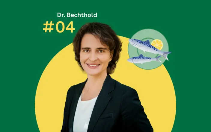 Dr. Angela Bechthold steht vor einem grünen Hintergrund. Rechts daneben ist ein blaugrüner Servierteller mit zwei Fischen zu sehen.