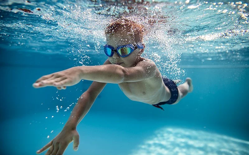 Ein Junge krault durch einen Pool, dabei trägt er eine Schwimmbrille.