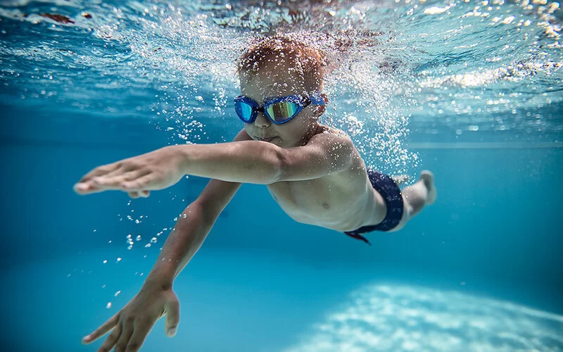 Ein Junge krault durch einen Pool, dabei trägt er eine Schwimmbrille.