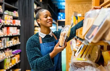 Eine Angestellte in einem Supermarkt sortiert in Folie verpackte Brotwaren in ein Regal.
