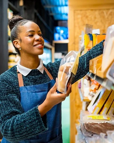 Eine Angestellte in einem Supermarkt sortiert in Folie verpackte Brotwaren in ein Regal.