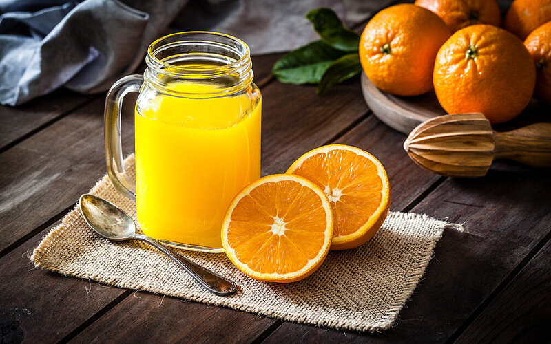 Frisch gepresster Orangensaft in einem Henkelglas, daneben eine aufgeschnittene Orange.