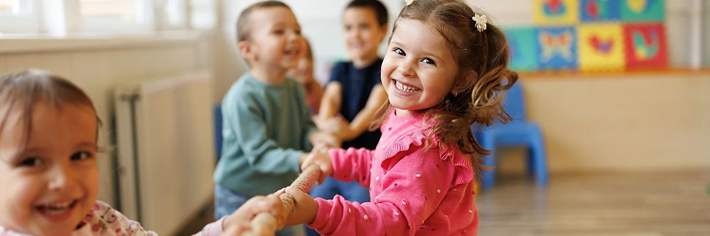 Vier Kinder ziehen im Kindergarten an einem Tau. Im Vordergrund sind zwei Mädchen zu sehen, im Hintergrund zwei Jungen.