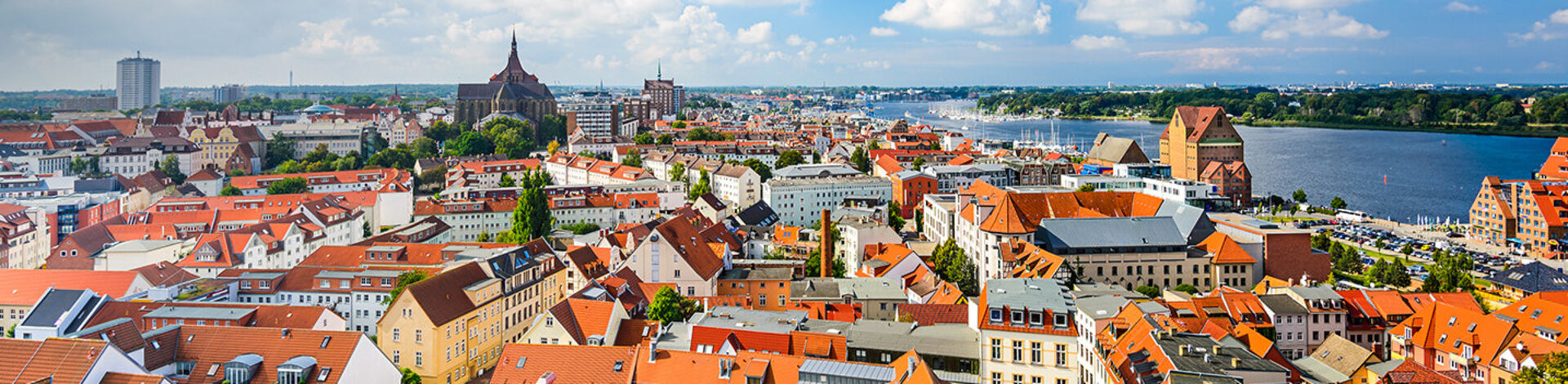 Zu sehen ist ein Panorama Bild der Skyline von Rostock bei sonnigem Wetter.