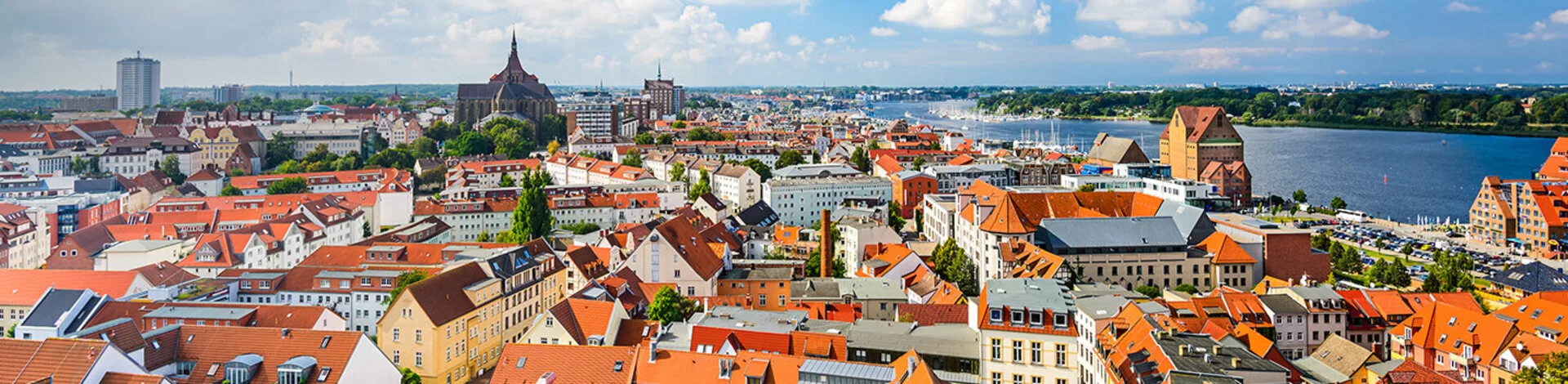 Zu sehen ist ein Panorama Bild der Skyline von Rostock bei sonnigem Wetter.