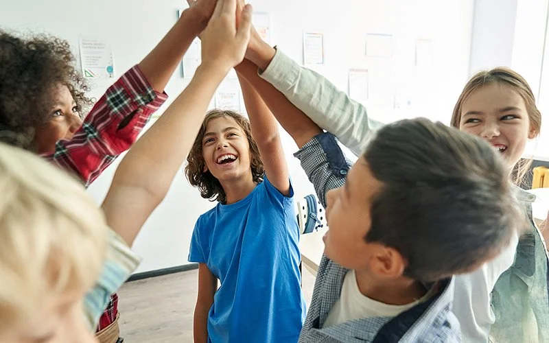Eine Gruppe von lächelnden Kindern legen ihre Hände in der Mitte zu einem High-Five zusammen.