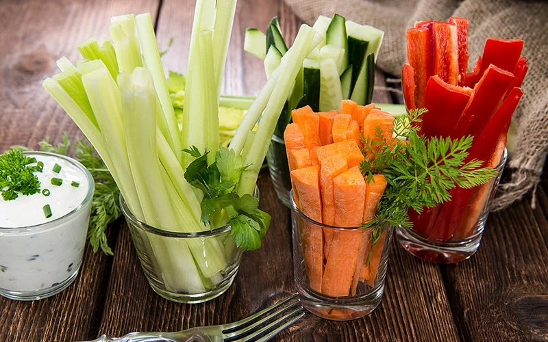 Verschiede Gemüsesticks in kleinen Gläsern stehen auf einem rustikalen Holztisch.
