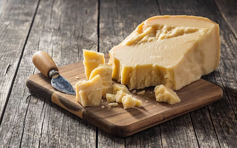Ein Stück Parmesan mit Käsemesser auf einem Holzbrett. Der Hartkäse ist für Menschen mit Laktoseintoleranz meist verträglich.