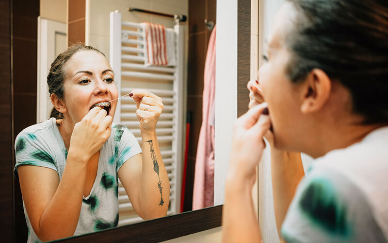 Eine junge Frau mit Brackets reinigt ihre Zahnzwischenräume mit Zahnseide.