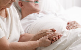 Alte Frau hält die Hand ihres sterbenden Partners in einem Hospiz.