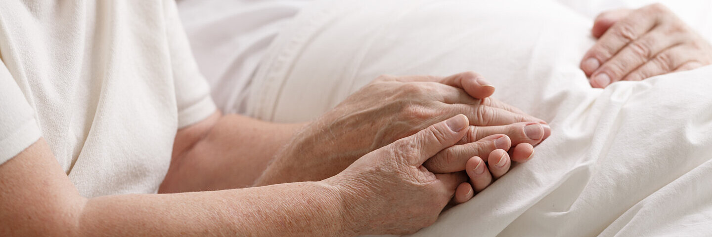 Alte Frau hält die Hand ihres sterbenden Partners in einem Hospiz.