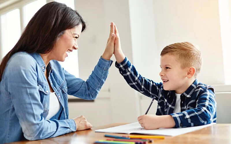 Mutter und Sohn arbeiten gemeinsam an den schlechten Schulnoten und klatschen sich nach erfolgreichem Erledigen der Hausaufgaben motiviert ab.