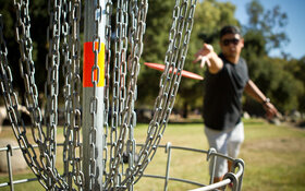 Ein Mann wirft beim Disc Golf eine Discgolfscheibe Richtung Korb.
