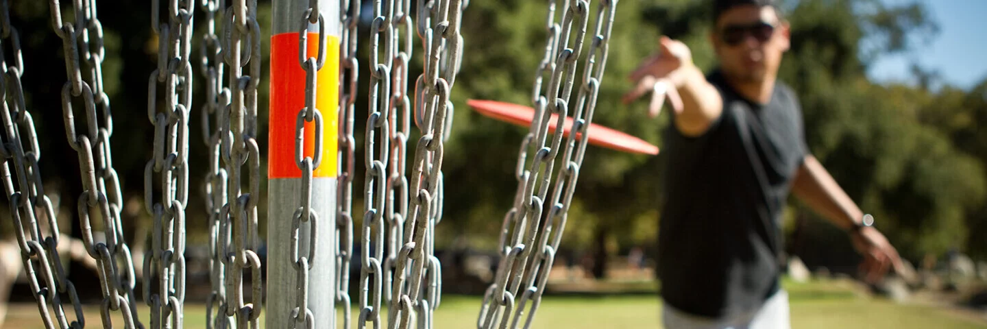 Ein Mann wirft beim Disc Golf eine Discgolfscheibe Richtung Korb.