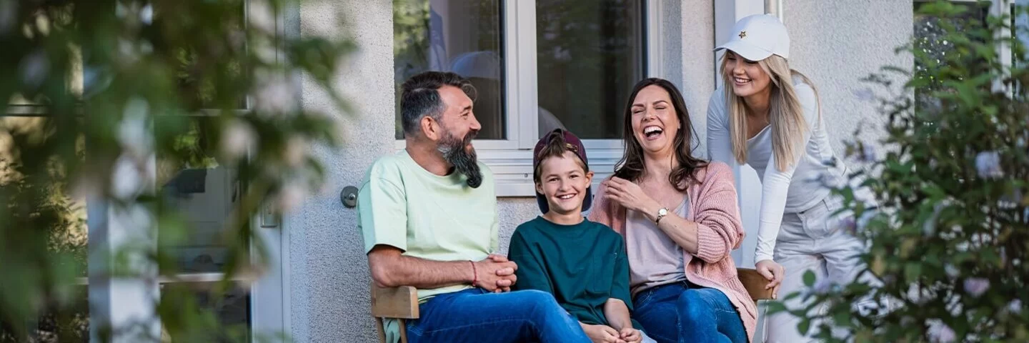 Eine Familie sitzt vor dem Haus auf einer Bank und lacht.