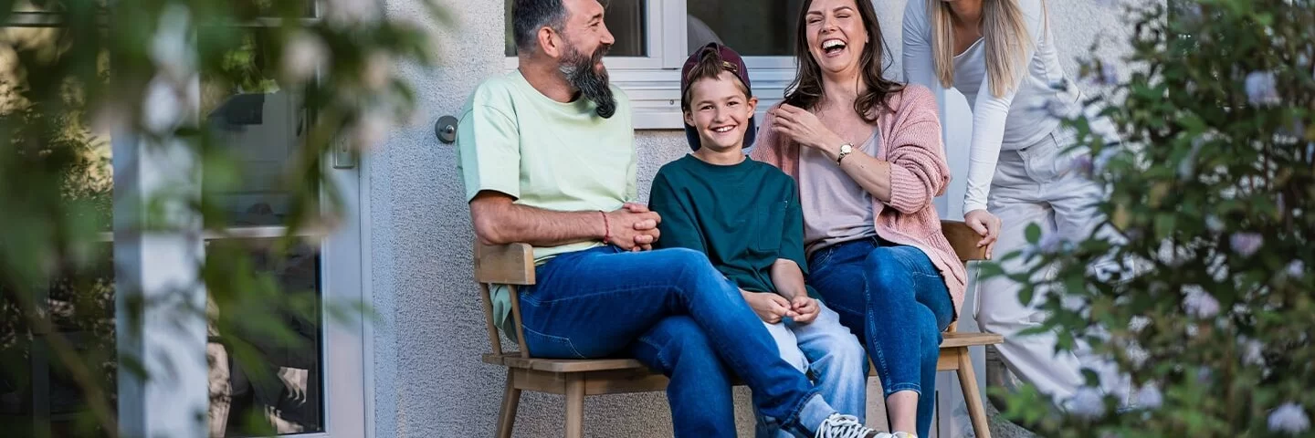 Eine Familie sitzt vor dem Haus auf einer Bank und lacht.