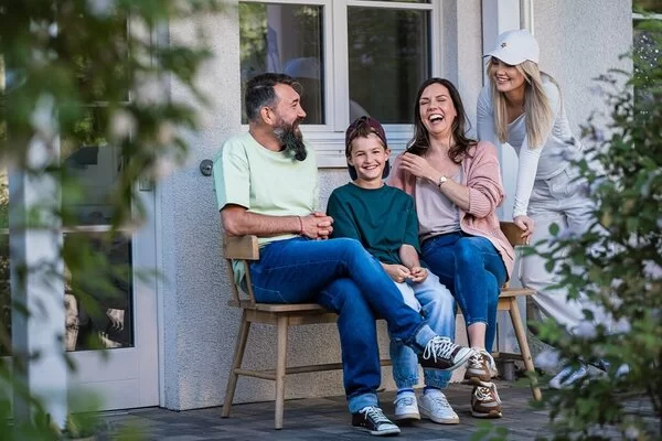 Eine Familie sitzt vor dem Haus auf einer Bank und lacht.