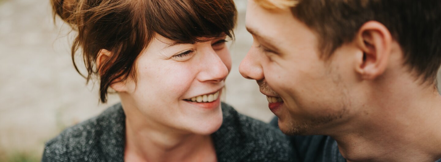 Eine junge Frau und ein junger Mann gucken sich in die Augen und lächeln.