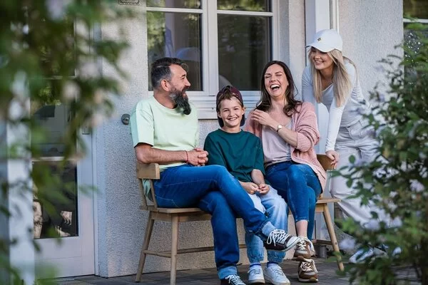 Eine Familie sitzt vor dem Haus auf einer Bank und lacht.