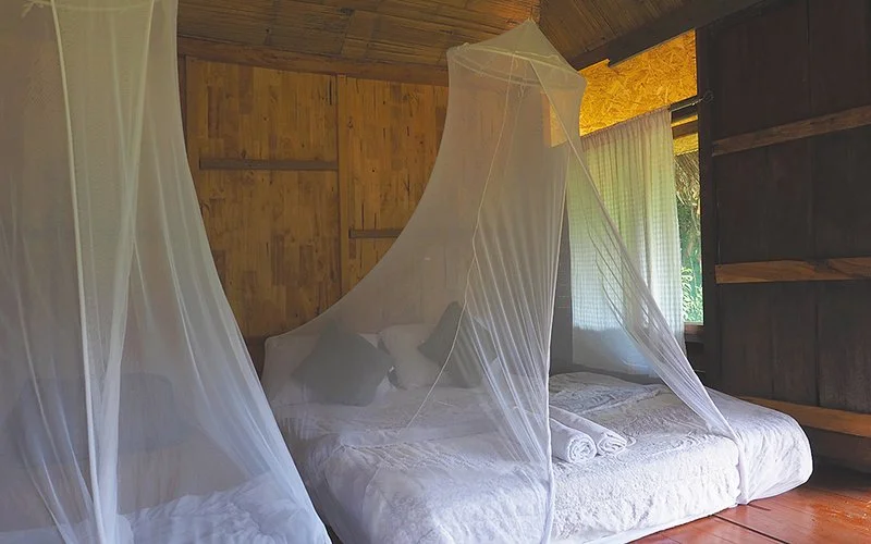 In einem Schlafraum eines Resorts hängen Moskitonetze über zwei großen niedrigen Betten.