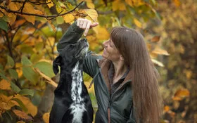 Melanie von Zelewski schaut lachend ihren großen, schwarzen Hund an, der neben ihr im herbstlichen Wald sitzt.
