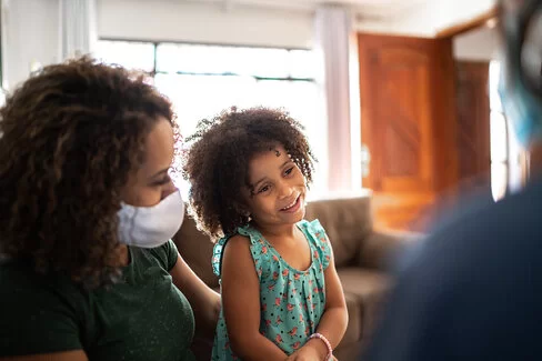 Ein Kind spricht zuhause mit einer medizinischen Person. Die sozialmedizinische Nachsorge hilft beim Übergang zwischen Krankenhaus oder Reha und der Familie.