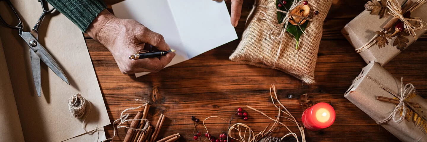 Ein Mann schreibt eine Weihnachtskarte und hat Geschenke nachhaltig verpackt.