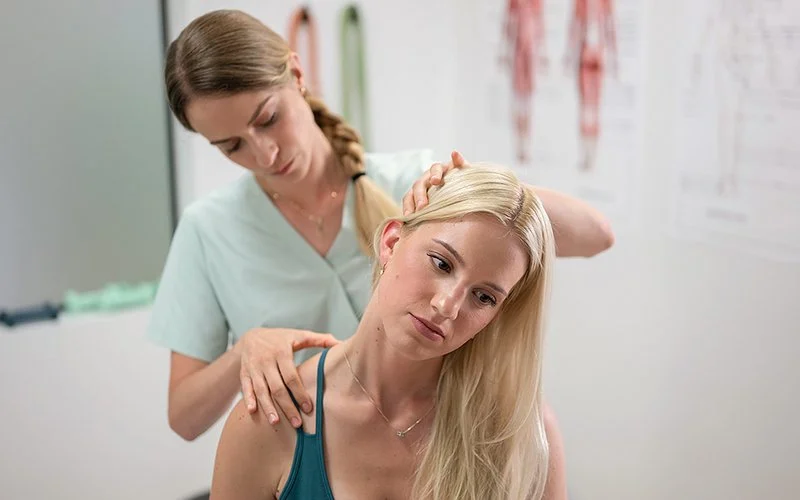 Eine Physiotherapeutin behandelt die Schulter einer jungen Frau.