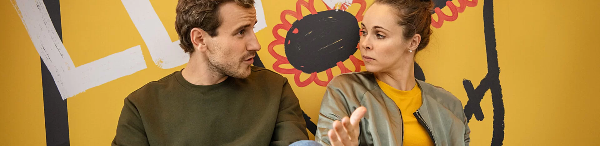 in junger Mann sitzt neben einer jungen Frau, schaut ihr offen in die Augen und redet mit ihr.
