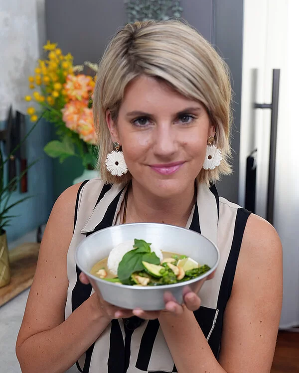 TV-Köchin Felicitas Then hält eine Schale mit einem Reisball und grünem Curry in ihren Händen und präsentiert diese freundlich lachend in die Kamera.